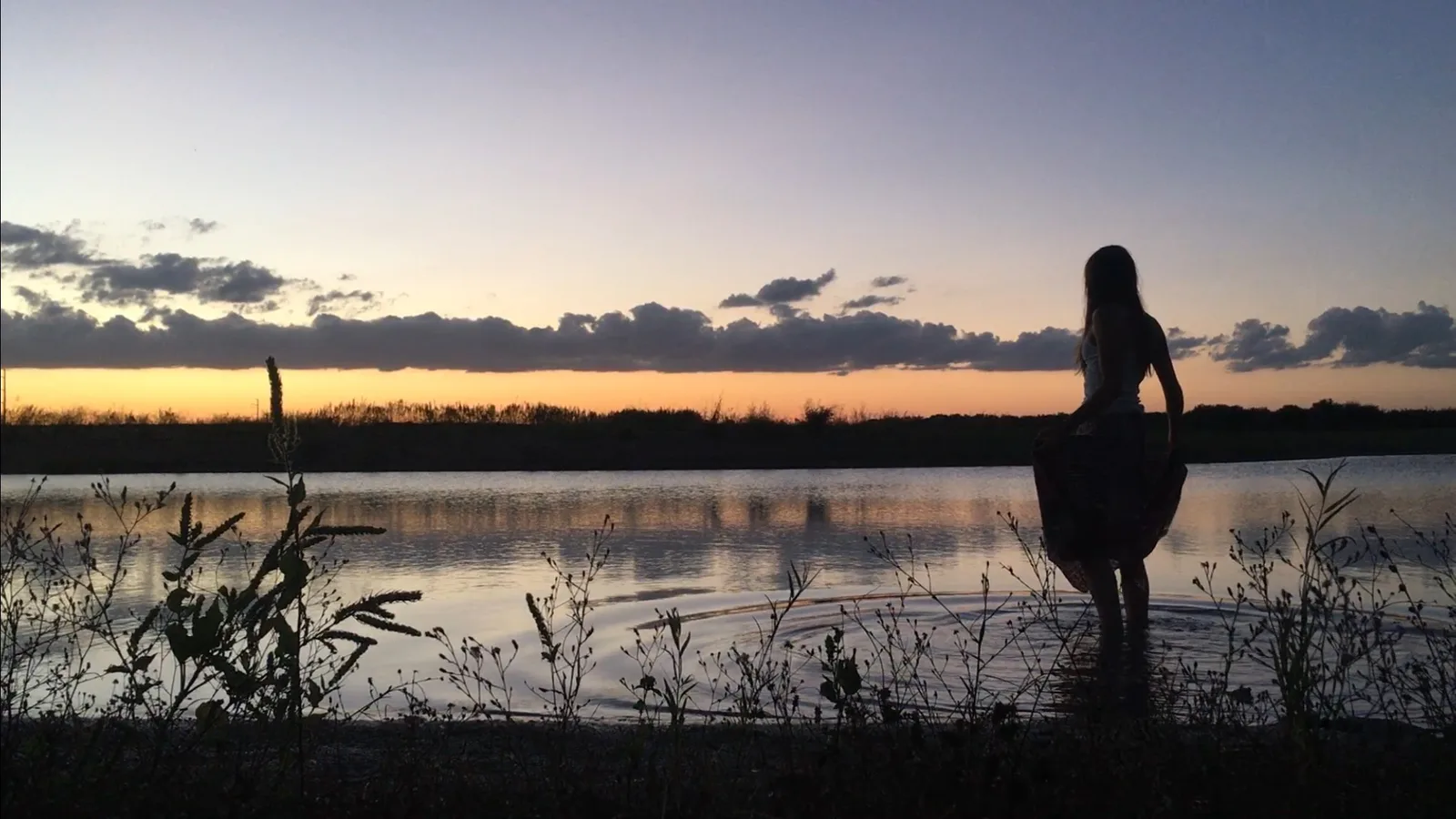 Silhouette of a woman standing in a lake at sunset.