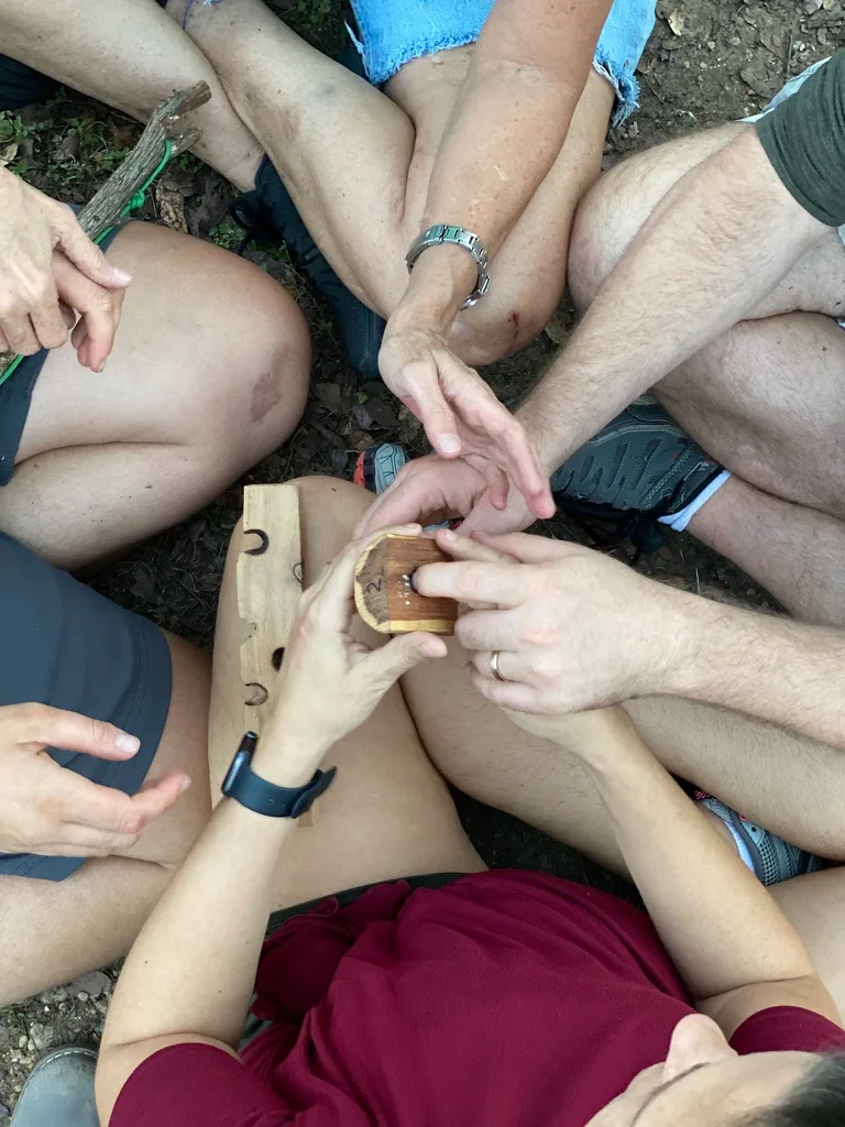 Seen from above, people sit close in a circle, their hands together on a small wooden object.